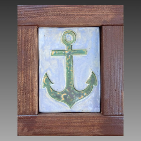 Handmade clay tile with a greenish anchor on a blue background. Set in a handmade brown wooden frame