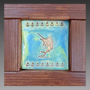 Clay artwork in a handmade frame. Art includes a sailfish leaping out of the water, with a border of small anchors. Background is painted in blue and green swirls.